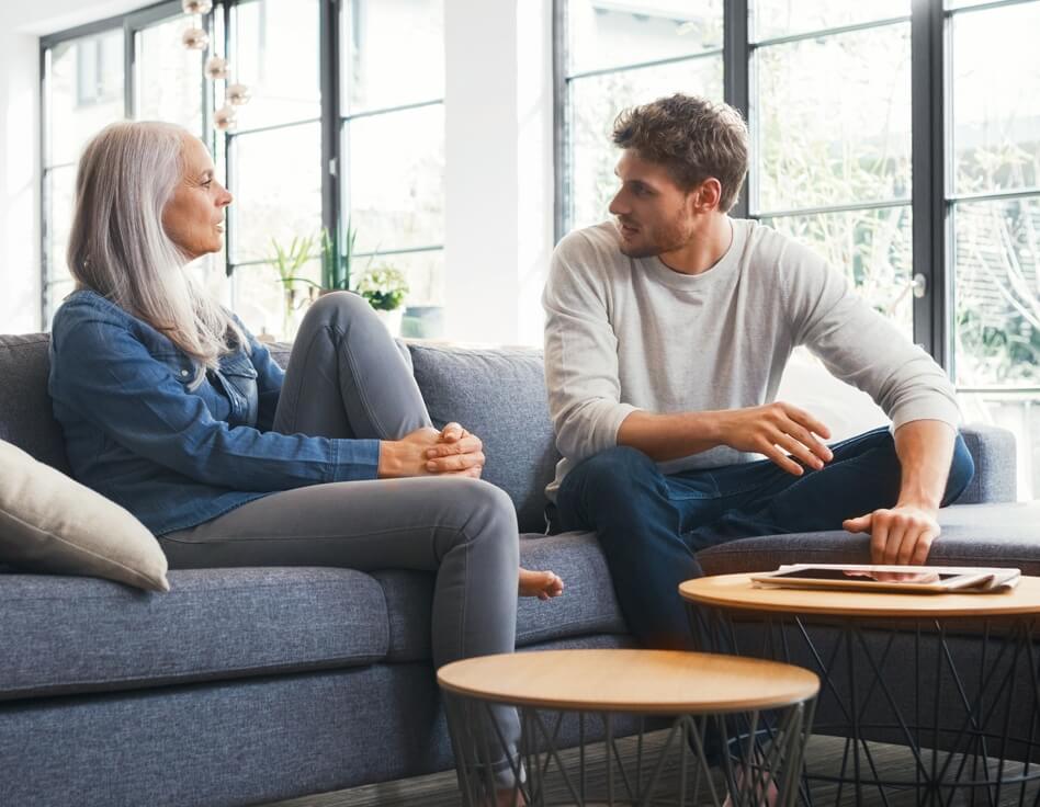 Eine an einer seltenen Erkrankung leidende Mutter sitzt mit ihrem Sohn, der sie unterstützt, auf einer Couch.